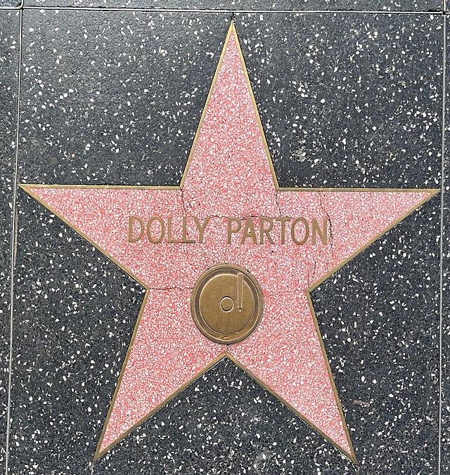 Dolly Parton's Imagination Library sends free books to children around the world. Pictured is Dolly Parton's star on the Hollywood Walk of Fame; a pink/salmon-colored star with Parton's name on it outlined in gold against a black background.